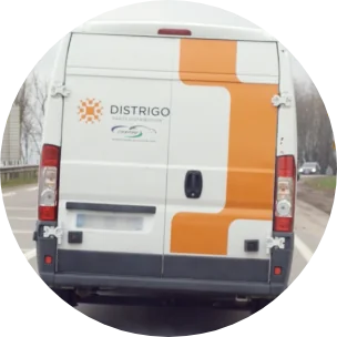 Achteraanzicht van een Distrigo-bestelwagen met oranje belettering, rijdend op een weg met bomen langs de kant.