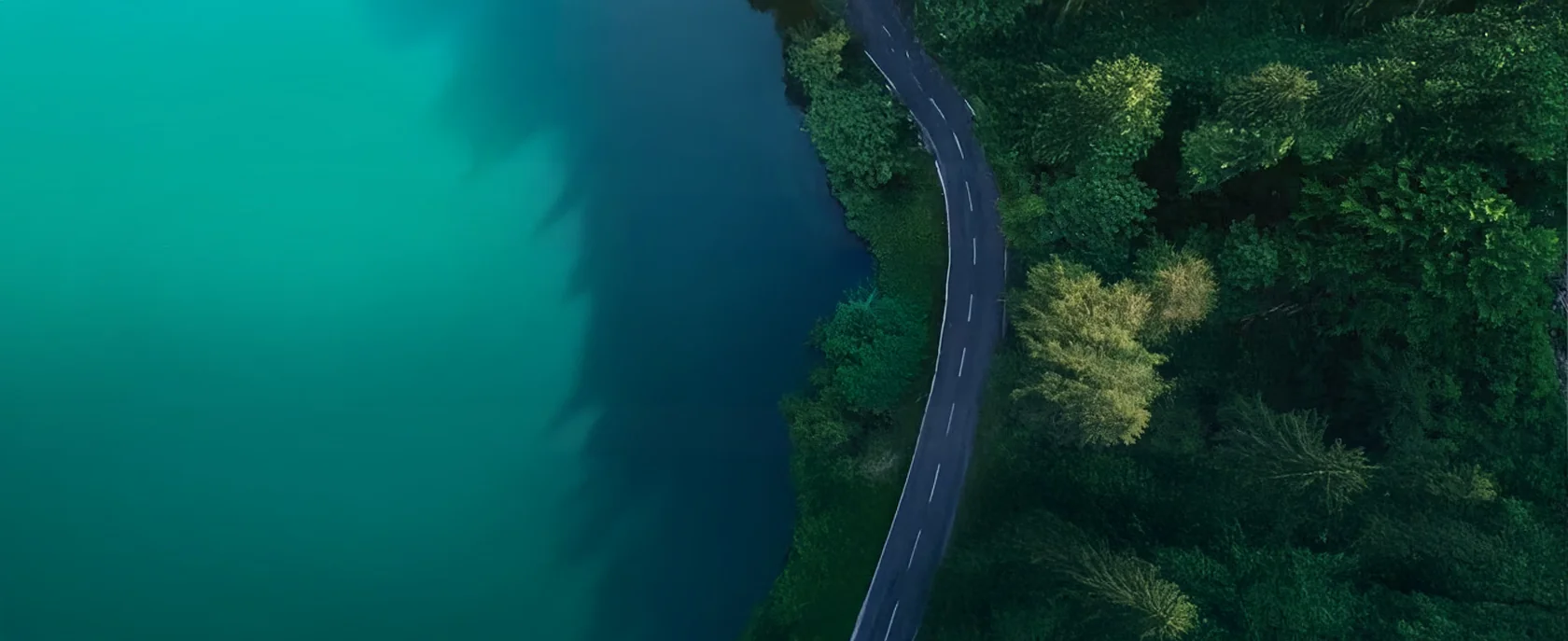 Luchtbeeld van een bochtige weg langs een turquoise meer en groen bos, symbool voor natuur en mobiliteit.